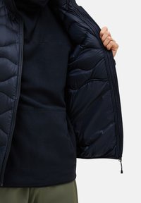 Navy blue insulated jacket with a quilted exterior, featuring a soft fleece interior. Zippered front and adjustable hem with drawstrings.