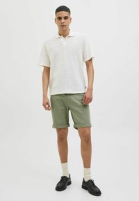 White knitted polo shirt with a subtle pattern, paired with olive green rolled shorts, white socks, and black shoes.