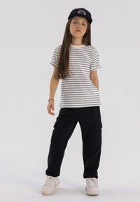 Wit en zwart gestreept t-shirt, zwarte cargobroek met zakken, witte sneakers en een zwarte pet. Eenvoudig, casual outfit ontwerp.