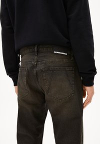 Jeans de mezclilla negra con un acabado desgastado, que presentan una cintura alta, cinco bolsillos y un parche rectangular en la parte trasera con el logo "ARMEDANGELS".