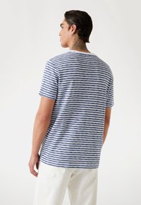 T-shirt en coton rayé bleu et blanc, manches courtes, col rond, coupe décontractée, avec un ourlet droit et de subtils fentes latérales.