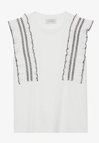 White short-sleeve top featuring ruffled black trim along the shoulders and decorative stitching. Soft fabric with a relaxed fit.