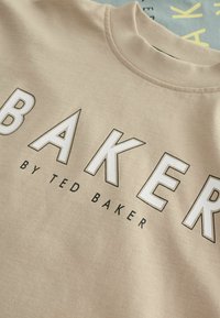 Beige-Sweatshirt mit auffälligem "BAKER"-Schriftzug in Weiß und Schwarz, rundem Halsausschnitt und strukturiertem Stoff.