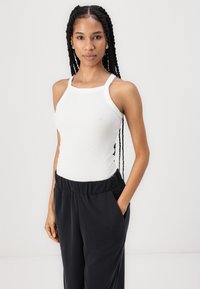 Valge ribaga tanktop, millel on ruudukujuline kaelus, koos mustade elastse vöökohtadega pükstega, millel on küljetaskud. Sujuv tekstuur, minimalistlik disain.