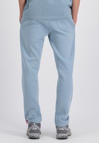 Lichtblauwe sweatpants van zachte stof, met een enkele achterzak en geribbelde manchetten, gecombineerd met grijze sneakers.