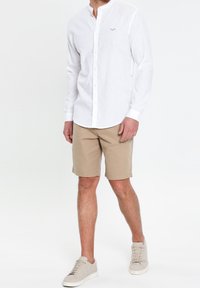 Chemise blanche boutonnée avec col officier, associée à un short beige. Des baskets blanches complètent la tenue. Tissu texturé et design simple.