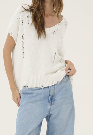 Top blanco de punto con tejido abierto, con un escote amplio y un corte ligeramente suelto. Combinado con jeans altos de cintura en un tono azul claro.