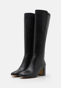 Bottes en cuir noir montantes avec un bout pointu, un talon carré, un design sans couture et un subtil détail de couture le long des bords supérieurs.