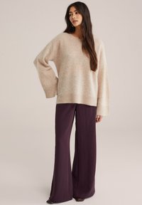 Beidzis, pārmērīgs adīts džemperis ar ribotām piedurknēm, apvienots ar brīviem, tumši plūmju platā stila biksēm. Abām apģērbu daļām ir mīksti faktūras.