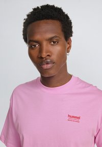 Lyserød bomulds t-shirt med rund hals, prydet med et rødt logo på venstre bryst. Kortærmet og afslappet pasform. Glat tekstur.