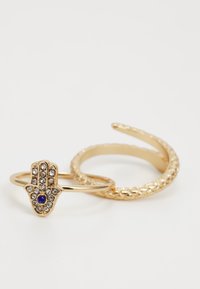 Gouden ringenset met een hamsa-ontwerp, voorzien van heldere stenen en een blauwe accent, samen met een gestructureerde band met een gedraaide afwerking.