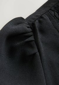 Tissu noir avec une surface texturée, présentant un détail froncé à la couture, mettant en avant la douceur et le tombé.