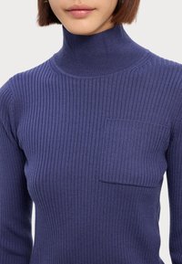 Geribbelde coltrui in donkerpaars, met een borstzak, gemaakt van een flexibele breisel, nauwsluitend ontwerp en zonder zichtbare sluitingen.