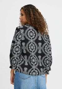 Blusa nera con motivi floreali bianchi, maniche lunghe con polsini arricciati e vestibilità rilassata. Realizzata in tessuto leggero.