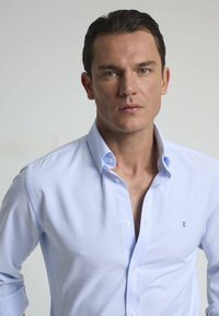 Camisa de hombre de color azul claro, con tejido suave, que presenta un cuello clásico, mangas largas y un pequeño logo de la marca cerca del pecho.