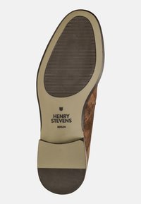 Semelle de chaussure en cuir suédé marron avec un grip en caoutchouc noir texturé ; comporte un logo et une forme incurvée avec une bordure d'accent en tan.