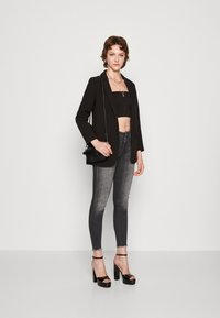 Black blazer over a black crop top, paired with distressed gray skinny jeans and black platform sandals. Accessories include a handbag.