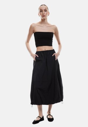 Haut court sans manches noir à côtes associé à une jupe midi noire fluide avec une taille élastique et des poches latérales. Porté avec des ballerines noires.