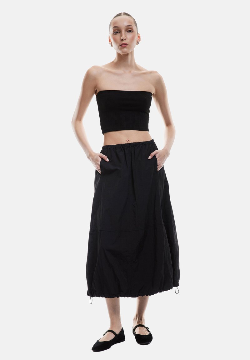 Top corto sin mangas de canalé negro combinado con una falda midi negra holgada que presenta una cintura elástica y bolsillos laterales. Llevado con zapatos planos negros.