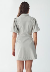 Hellgraues Kleid mit kurzen Puffärmeln, einem kragenförmigen Ausschnitt und einer taillierten Taille; glattes Material und Oberkante des Knies.
