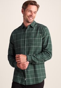 Dark green checkered shirt made of soft fabric. Features a button-up design, long sleeves, chest pocket, and subtle branding detail.