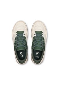 Light cream sneakers with green accents, perforated toe, flat laces, and branding on the tongue. Rubber sole with rounded edges.