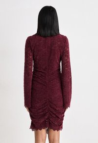 Burgundin pitsikleid, millel on pikad varrukad, kogutud detailid seljal ja laineline äär. Tekstureeritud lillemuster kogu kleidi ulatuses.