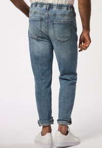 Joggers de mezclilla azul claro con cintura elástica, puños doblados y dos bolsillos traseros, combinados con zapatillas deportivas blancas.