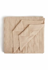 Beige strikket tæppe med et kabelstrik mønster. Det har et foldet hjørne, der afslører et struktureret væv og en frynse kant.