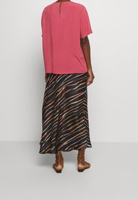 Rosa blus med korta ärmar och öppning baktill, kombinerad med en svart kjol med livliga orange och beige vågiga ränder. Bruna sandaler med flat sula.