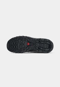 Black rubber sneaker sole with a rugged tread pattern and a red accent. Features deep grooves for traction and stability.