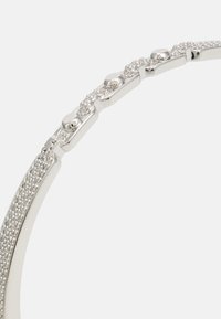 Gros plan d'un segment de bracelet en argent avec des maillons lisses et de petites pierres précieuses rondes et transparentes incrustées sur un fond clair.