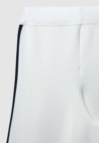 Tessuto bianco effetto texture, design affusolato con dettagli laterali neri. Vita elasticizzata e tasche, che mettono in evidenza uno stile atletico moderno.