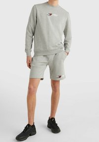 Szara bawełniana bluza z okrągłym dekoltem i logo, połączona z dopasowanymi szarymi szortami. Czarne buty sportowe podkreślają swobodny strój.