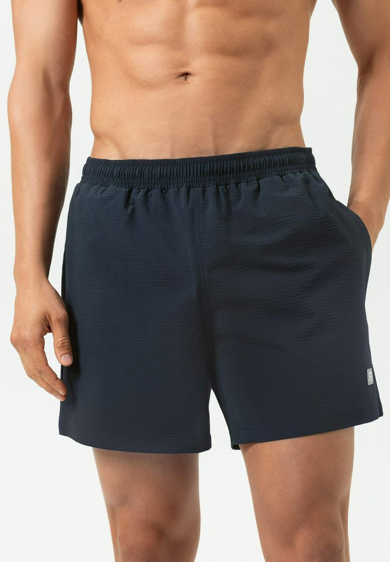 Shorts de bain bleu marine avec une ceinture élastique, un tissu texturé et des poches latérales. Le tissu présente un motif subtil. Ajustement réglable.