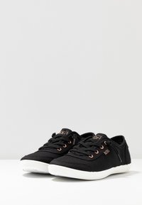 Black canvas sneakers with white rubber soles, featuring rose gold eyelets and branding. Classic low-top design and textured fabric.