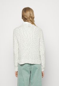 Hellgrauer Strickpullover mit strukturiertem Muster, ausgestattet mit gerippten Bündchen und Saum. Von hinten betrachtet, getragen über grünen Cordhosen.