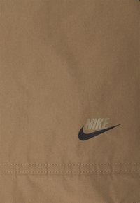 Brown fabric with a smooth texture features a black Nike logo. The stitching is visible along the bottom seam, adding detail.