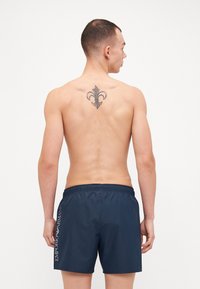 Shorts de bain navy avec une taille élastique, ornés d'un logo imprimé sur le côté et d'une texture lisse et légère. Pas de motifs ou d'accents supplémentaires.