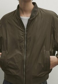 Olivegrüne Bomberjacke aus einem glatten, leichten Material. Verfügt über einen Reißverschluss vorne, einen gerippten Kragen und seitliche Taschen.