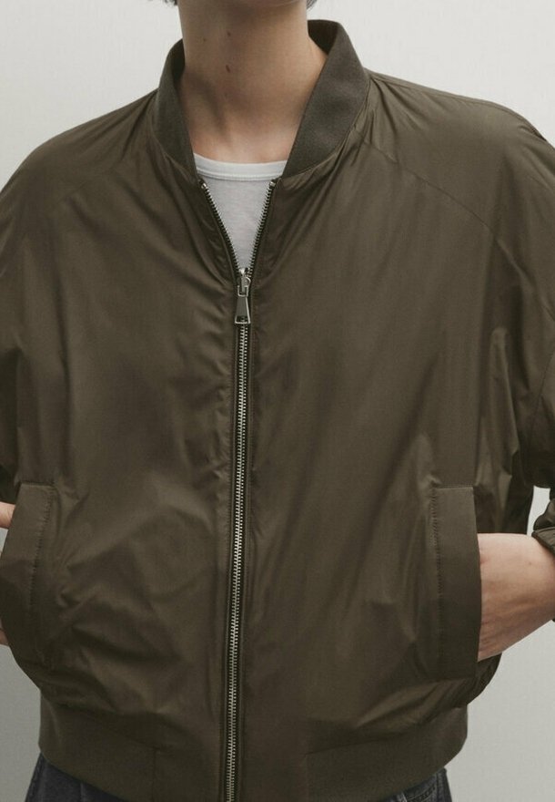 Olivegrüne Bomberjacke aus einem glatten, leichten Material. Verfügt über einen Reißverschluss vorne, einen gerippten Kragen und seitliche Taschen.