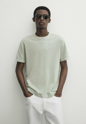 Mint green short-sleeve T-shirt made of soft fabric, featuring a crew neckline and relaxed fit. White pants and sunglasses worn.