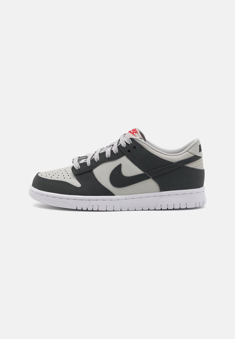 Las zapatillas Nike Dunk Low cuentan con un upper de cuero gris con acentos de cuero negro, una media suela blanca, cordones grises y una etiqueta de marca roja.