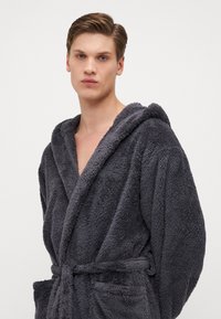 Grå plush badekåpe med hette, med sjalkrage, belte i midjen og to frontlommer, laget av myk, teksturert stoff.