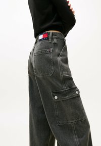 Jeans cargo grises con un ajuste relajado, múltiples bolsillos y una etiqueta de marca en la parte trasera de la cinturilla. Fabricados en denim con un acabado texturizado.