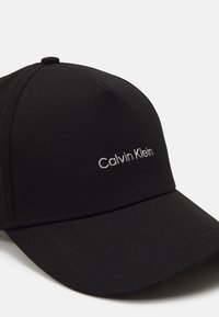Svart baseballkeps i texturerad väv, med en böjd skärm och broderad "Calvin Klein"-logotyp i silver på framsidan.