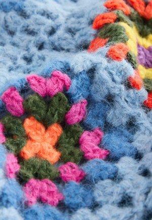 Crochet blanket featuring vibrant hexagonal patterns in pink, orange, green, and blue yarn. Soft texture with fluffy fiber details.