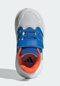 Dziecięce buty sportowe z białą siateczkową cholewką, niebieskimi akcentami i pomarańczową wkładką. Wyposażone w niebieski pasek na sznurowadłach zapewniający pewne dopasowanie.