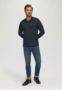 Langsleeve poloshirt in donker marineblauw, gemaakt van zachte stof, met een drieknoopsluiting. Gecombineerd met blauwe spijkerbroek en zwarte sneakers.