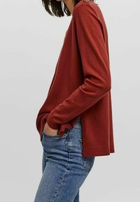 Maglietta a maniche lunghe bordeaux con vestibilità rilassata, realizzata in tessuto testurizzato. Abbinata a jeans in denim azzurro chiaro, con tasche laterali.